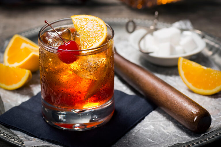 Old Fashioned Cocktail in a Dark Vintage Bar with Ingredients in Background